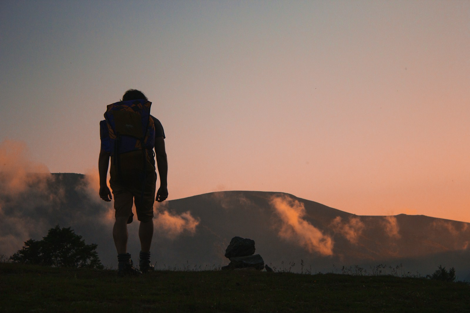 silhouette of man walking along field leading to mountain