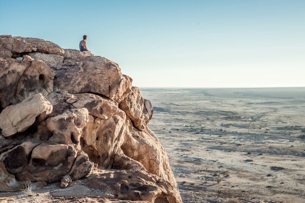 man sitting on top of rock formation near beach