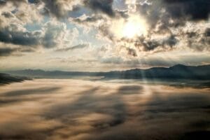 Blog Captivating view of the sun breaking through clouds over a mist-covered mountain range.